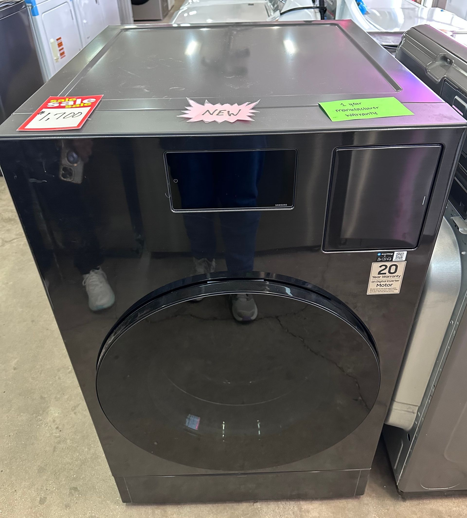 A black front-load washing machine with price tags attached, displayed in a retail appliance store.