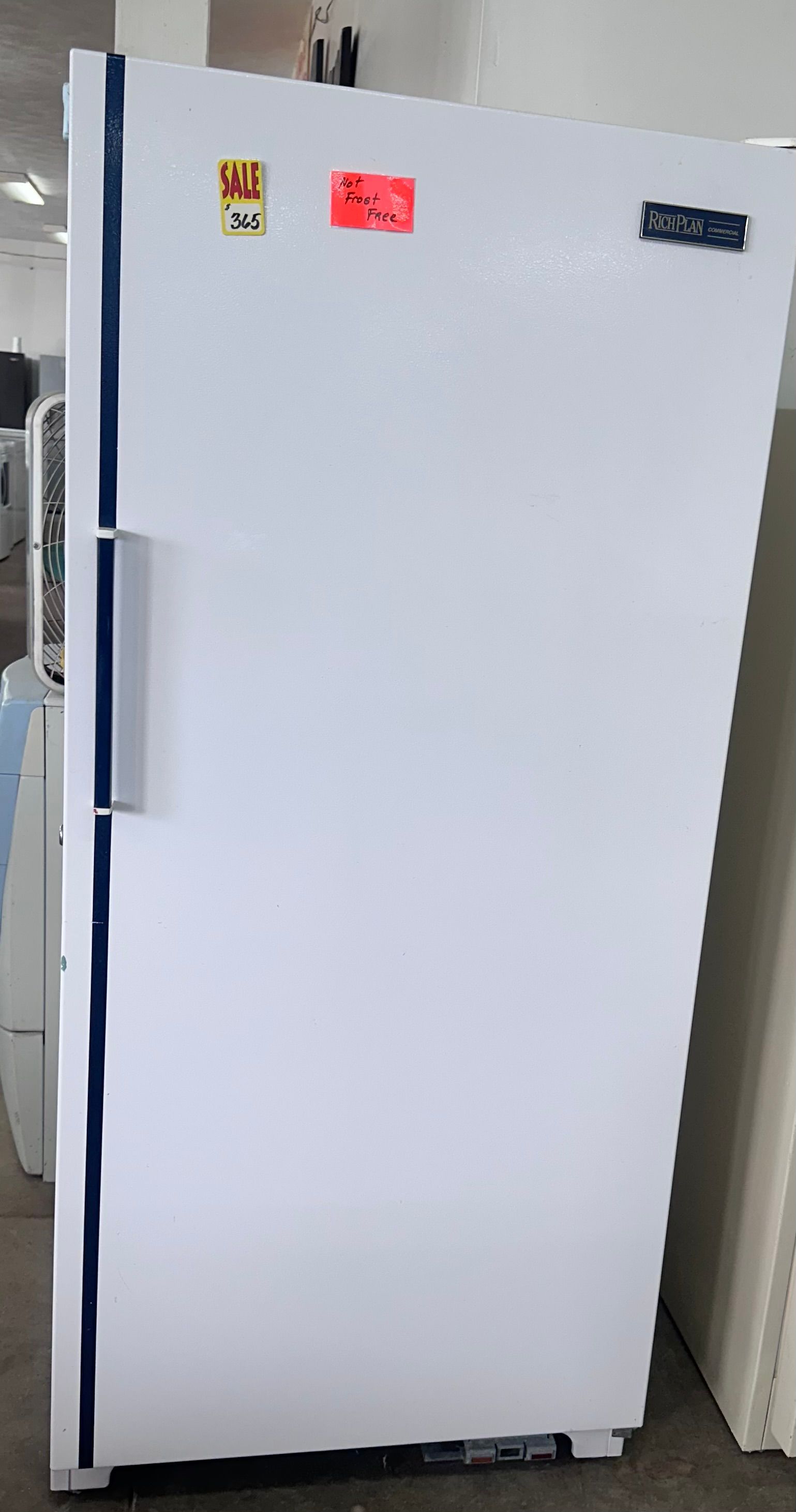 White refrigerator with a few magnets on the top front, standing beside a wall.