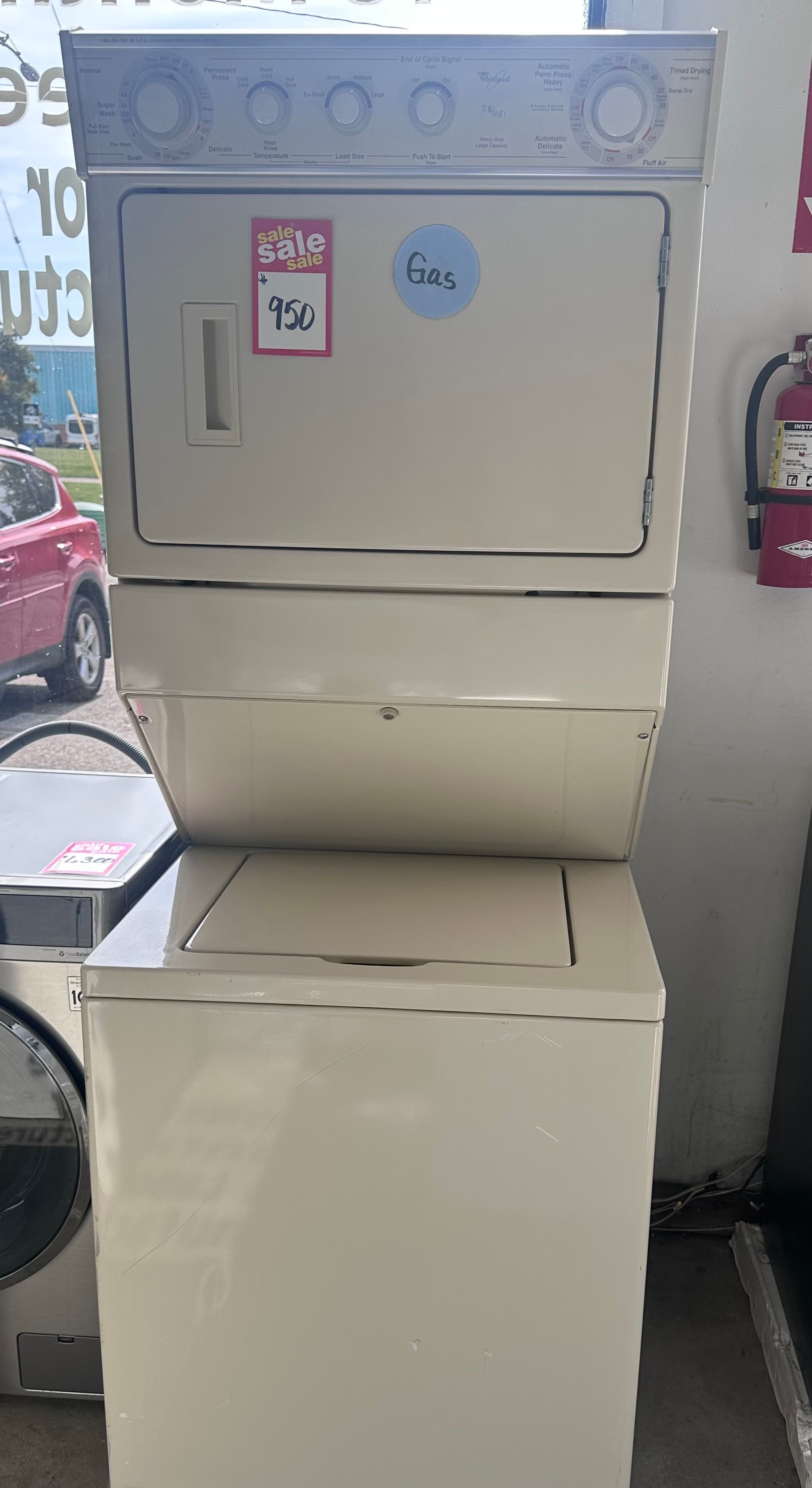Stacked beige washer and dryer, for sale, with price tags, indoors.