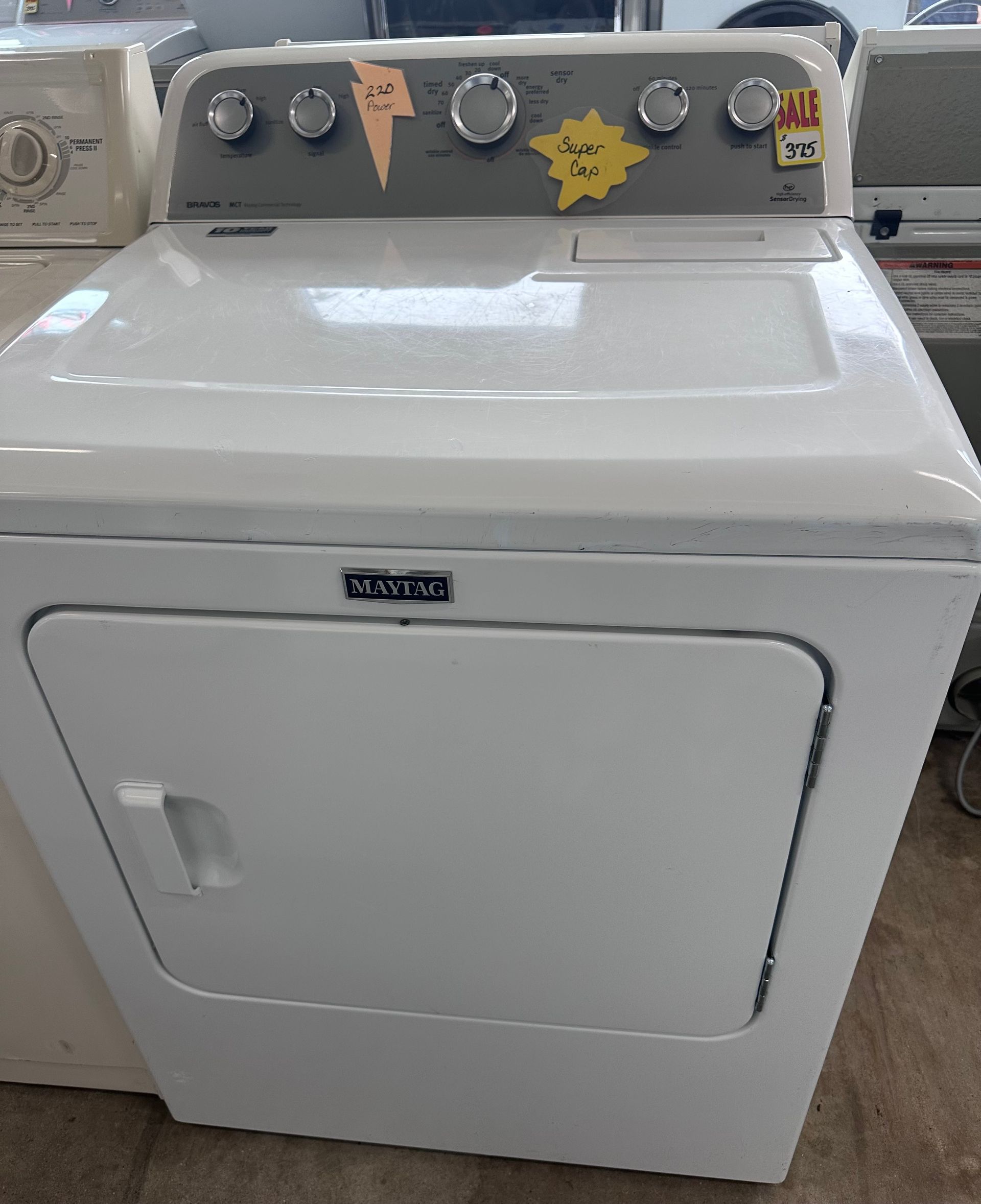 A white dryer is sitting on top of a wooden floor.