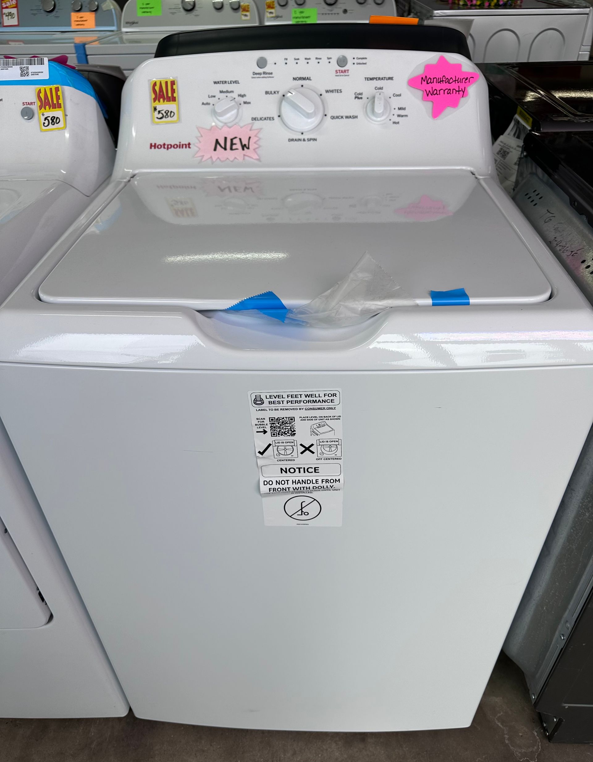 A new, white top-loading washing machine with control dials, displayed in a retail showroom.