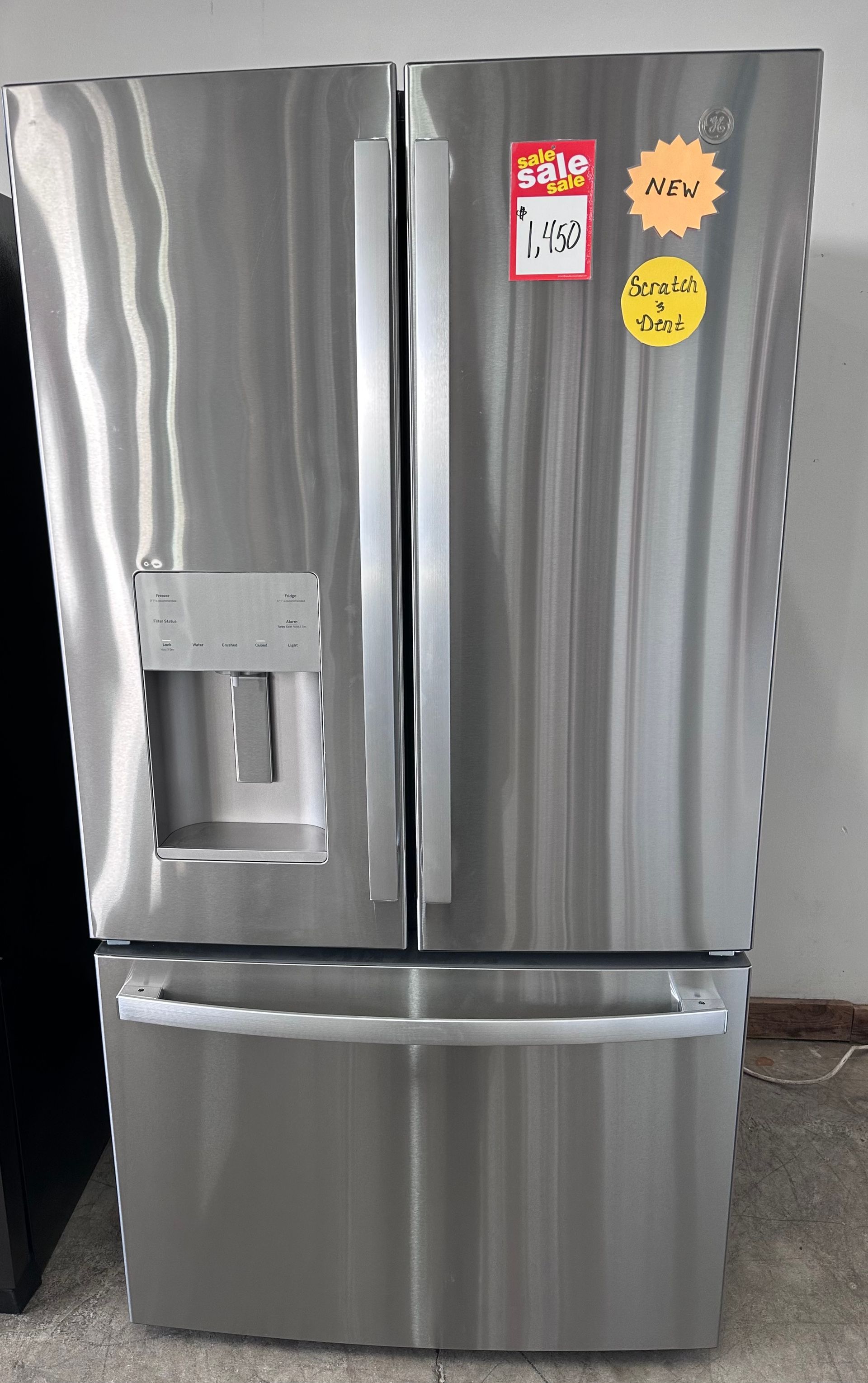 A stainless steel, French-door style refrigerator with a water dispenser on the left door and a bottom freezer drawer.