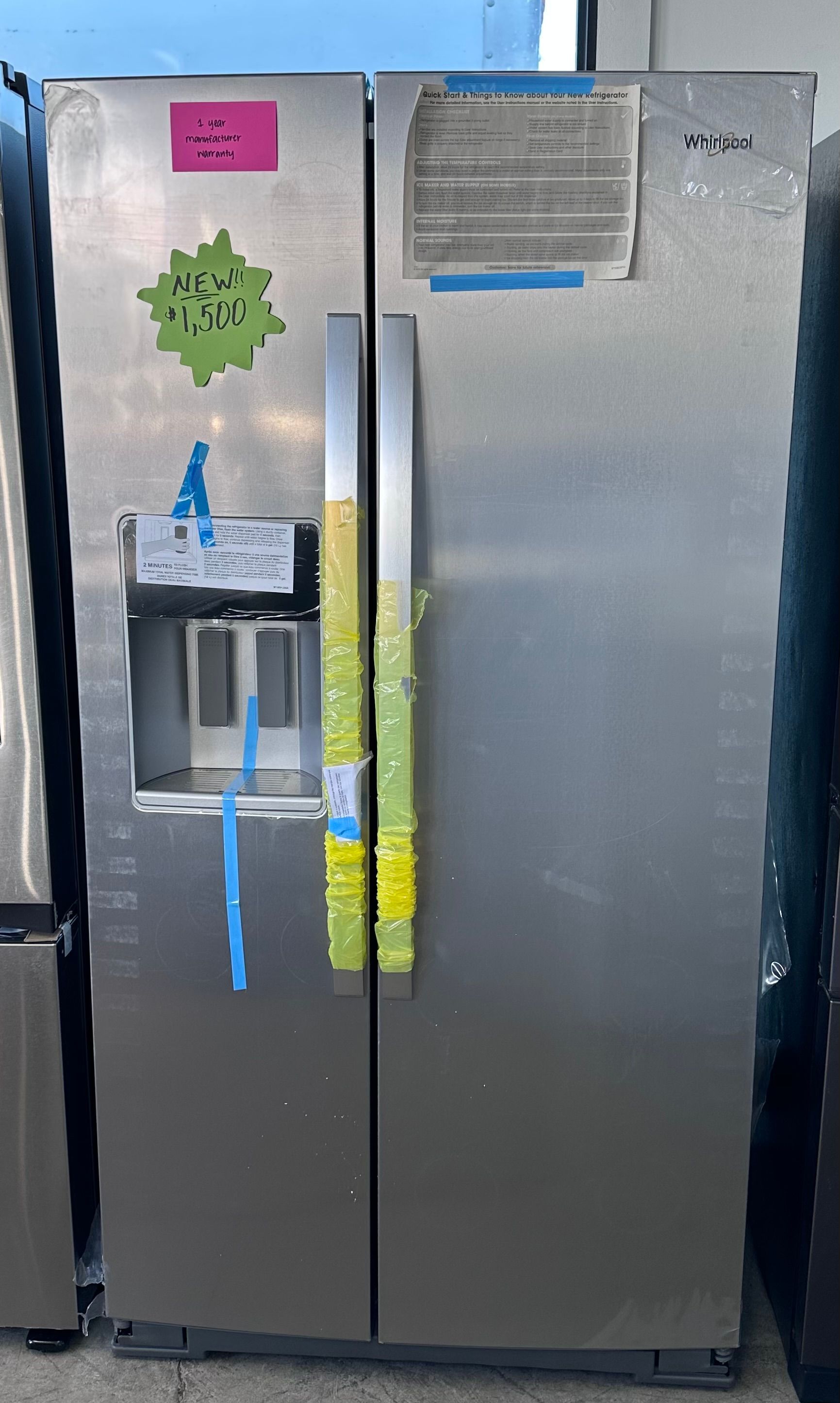 A stainless steel side-by-side refrigerator with a water dispenser, taped doors, and price labels attached.