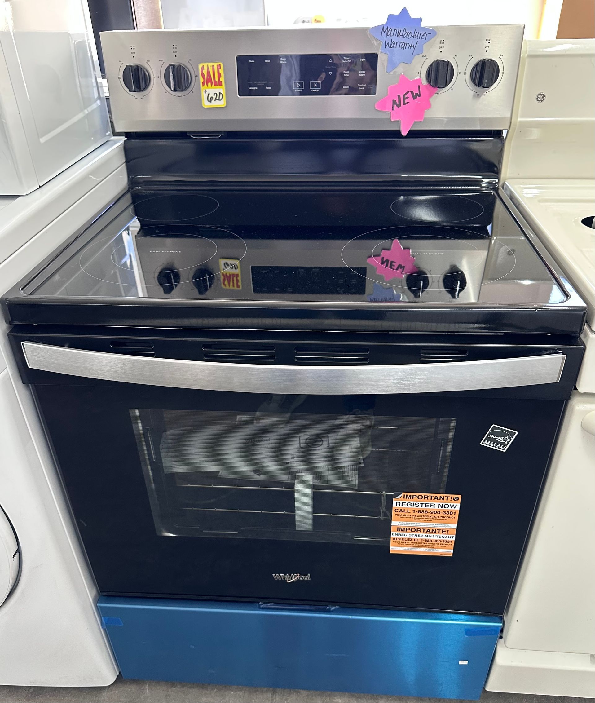 A stainless steel and black Whirlpool electric range with a glass cooktop, sitting in a retail showroom.