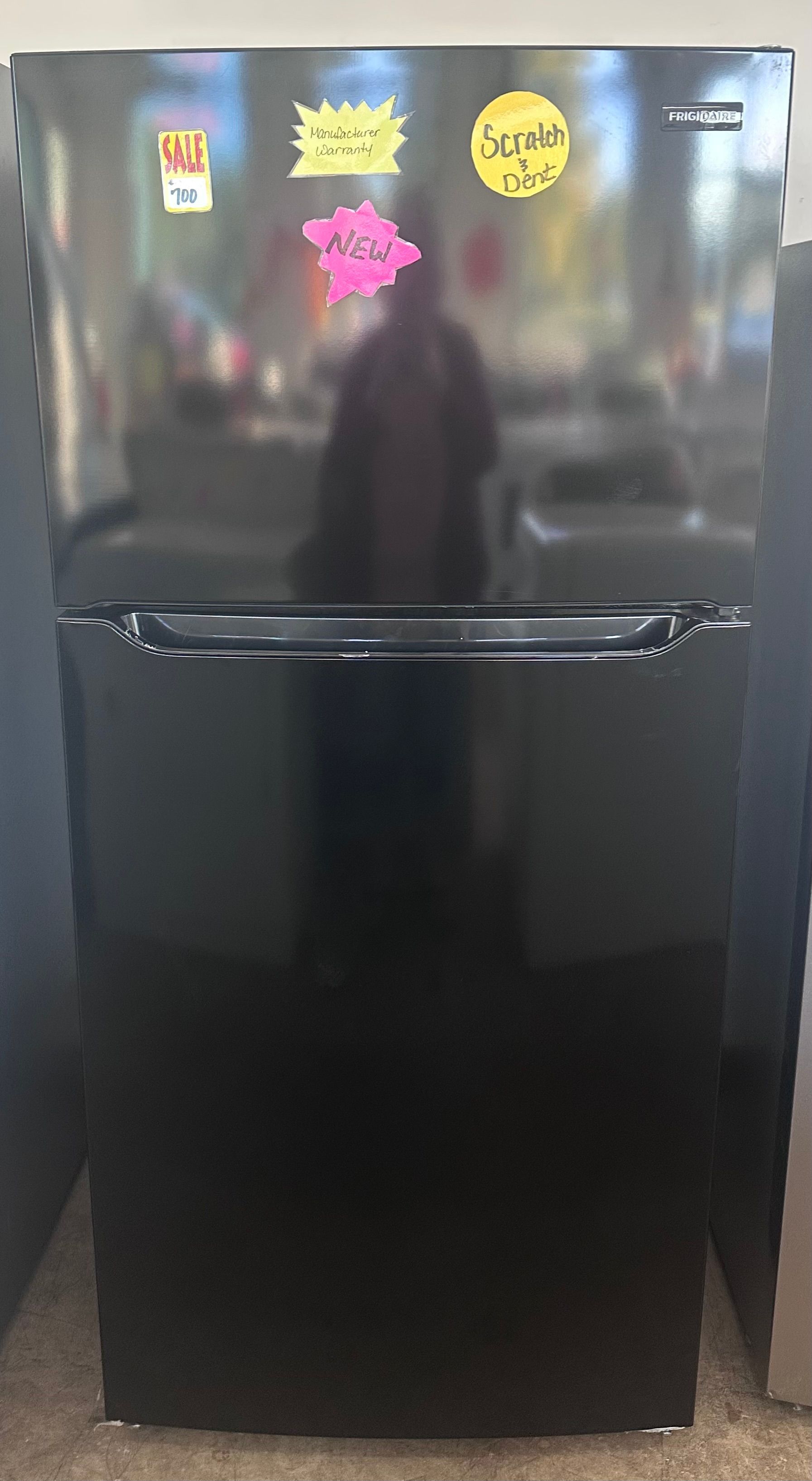 Black refrigerator with stickers on the door in a brightly lit setting.