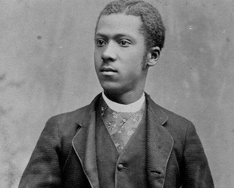 Portrait of a man in a dark suit with a patterned vest, looking to the side.