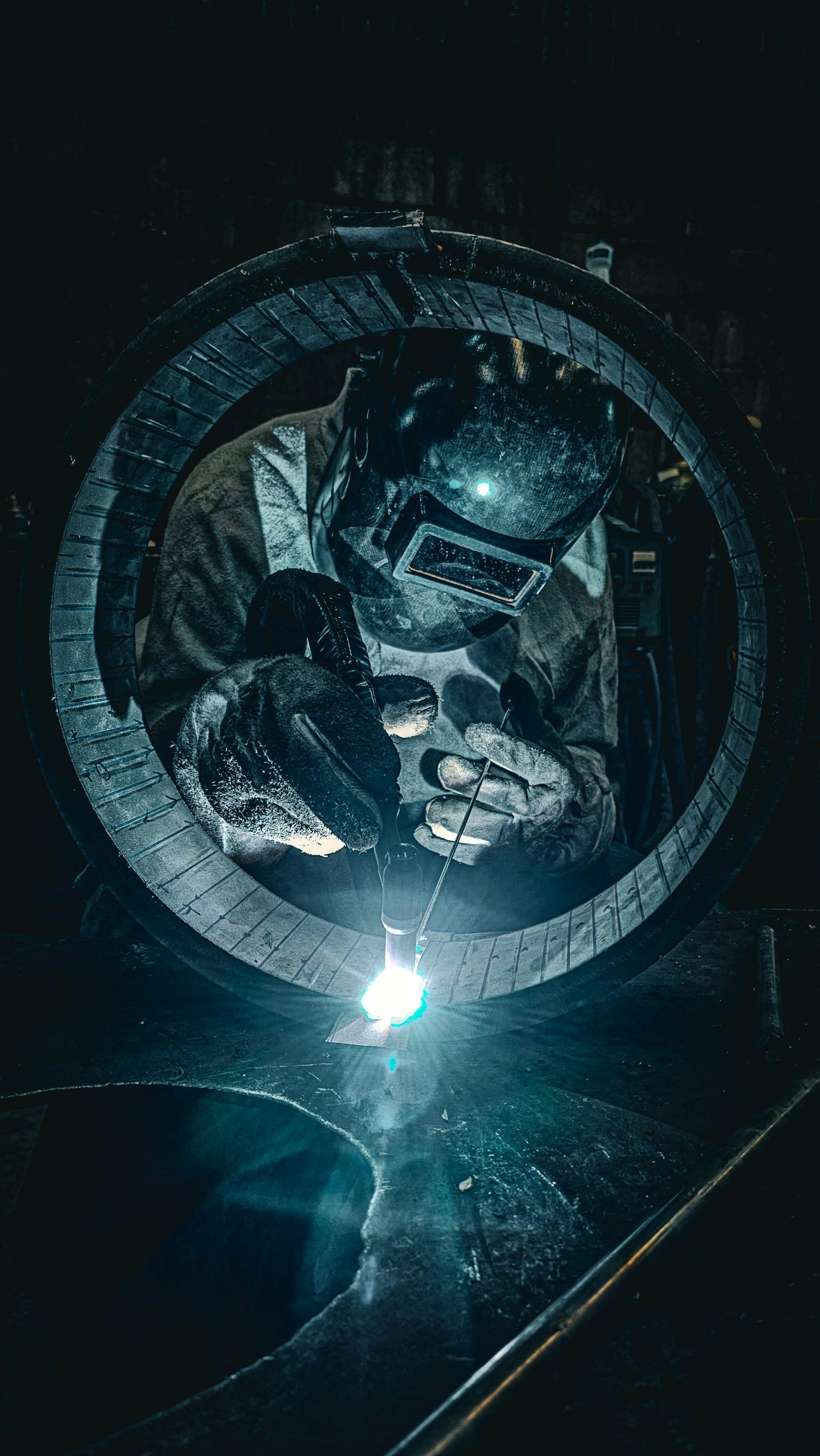 Welder inside large metal ring, welding. Sparks and bright light are visible.