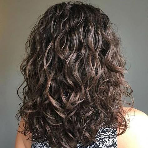 Mujer con cabello largo y rizado, castaño oscuro, hasta los hombros, con rizos definidos.