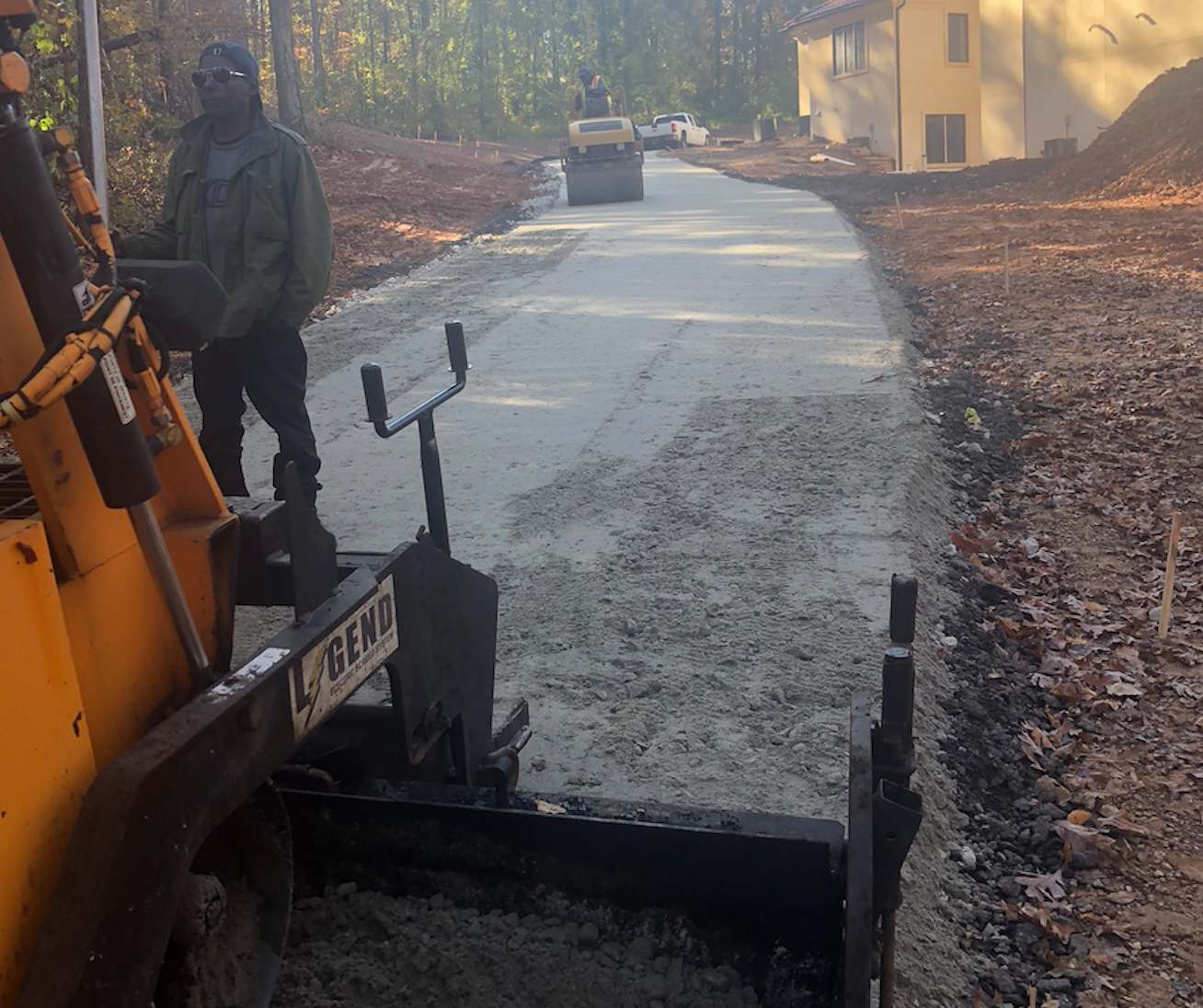 workers arranging fresh asphalt mix with rakes and shovel to patch a bump in the road