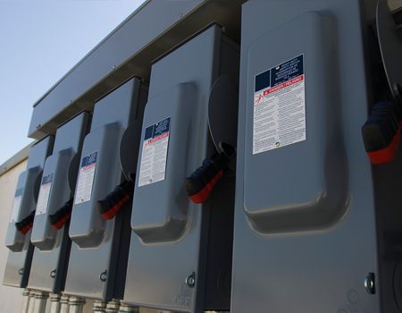 Row of gray outdoor electrical panels mounted on a building wall