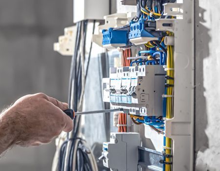 Hand using a screwdriver to wire an electrical breaker panel with blue components