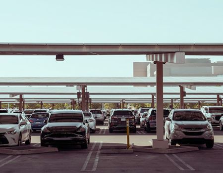 Cars parked in a covered lot under solar panels, viewed from the front.