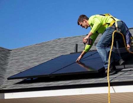 Worker installing solar panels on a rooftop under a clear blue sky