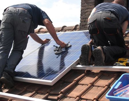 Worker installing solar panels on a shingled roof under a clear blue sky
