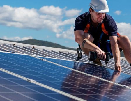 Technician installing solar panels on a rooftop under a blue sky