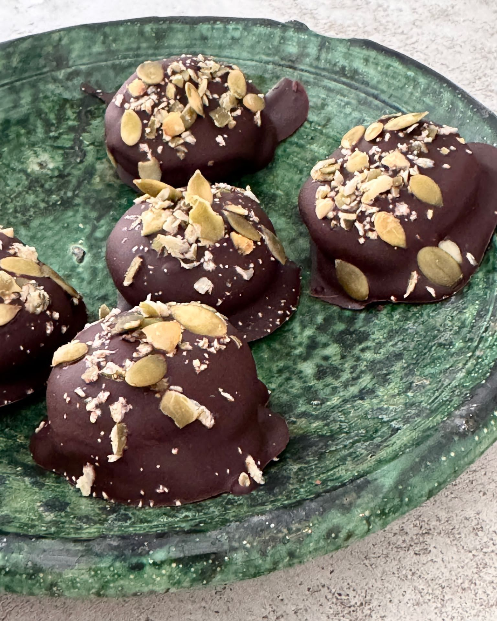 Chocoladeschildpadjes met pompoenpitten op een groen keramisch bord.