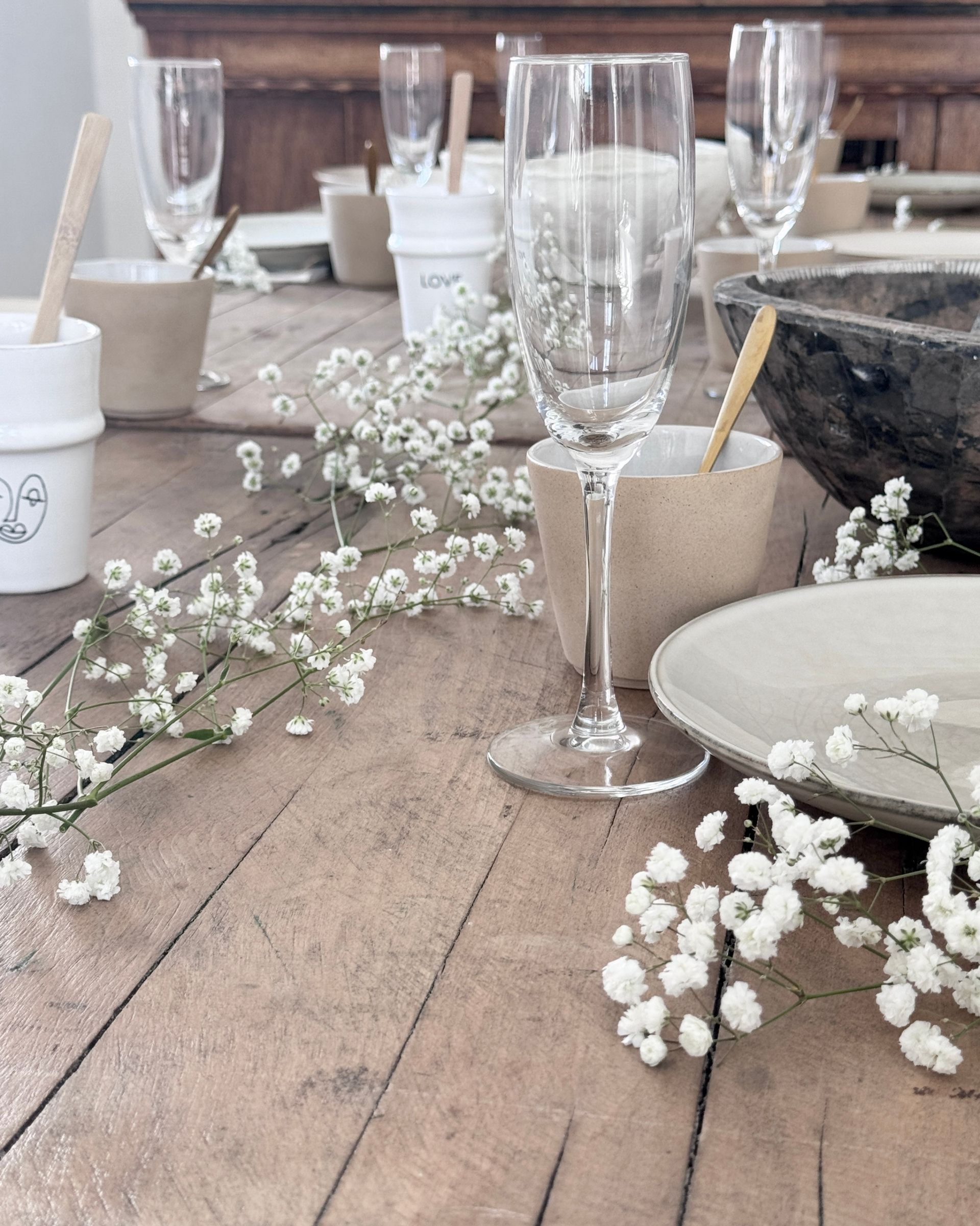 Tafeldekking met champagneglazen, borden en gipskruid op een houten tafel.
