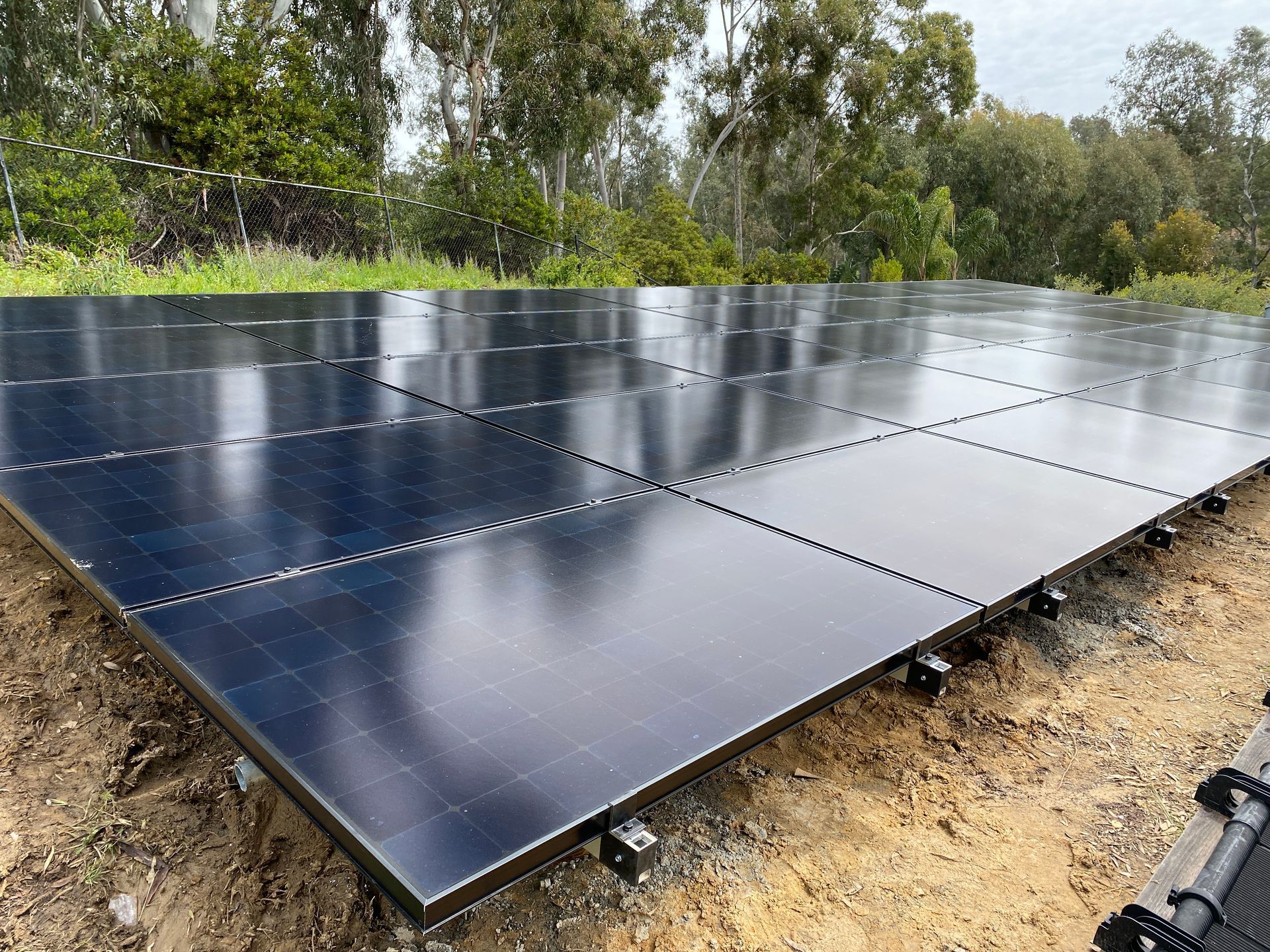 A row of solar panels are sitting on top of a dirt field.