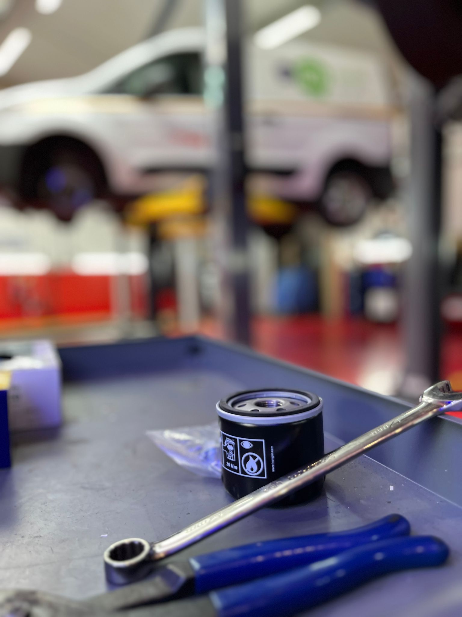 A wrench and pliers are on a tray in a garage with a car in the background.