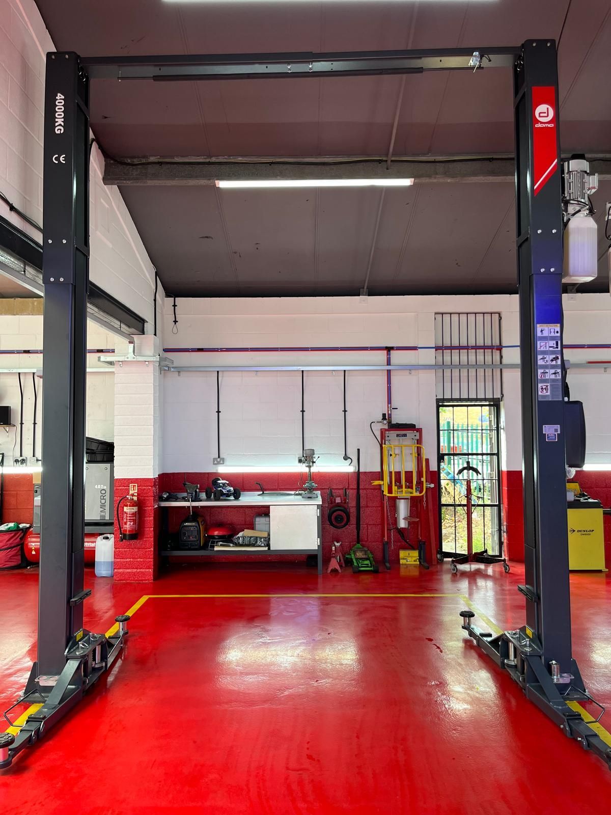 Two hydraulic lifts are in a garage with a red floor.