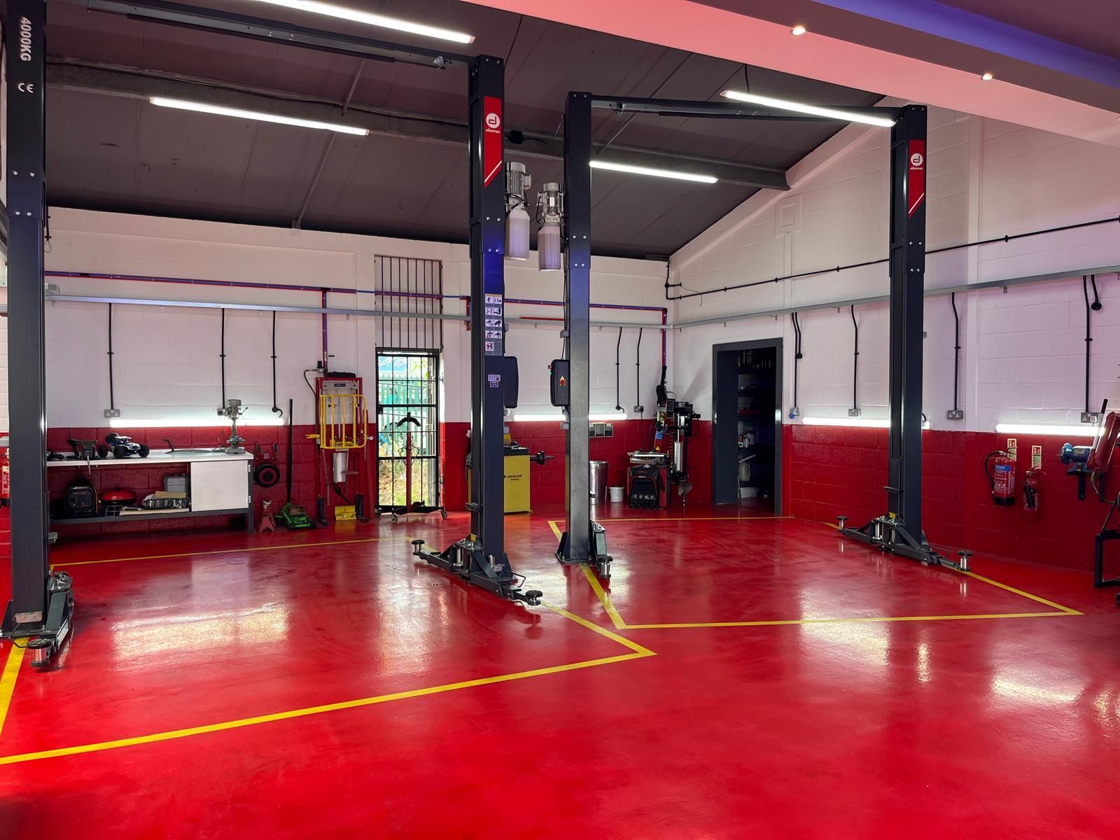 A garage with red floors and two lifts in it.