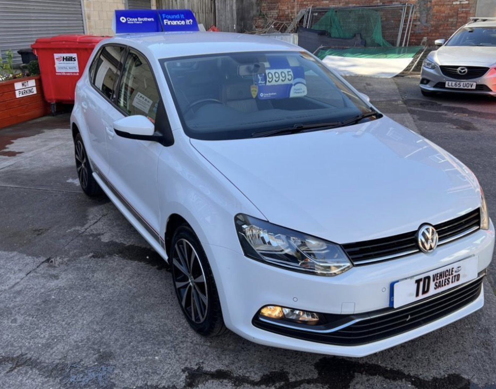 A white volkswagen polo is parked in a parking lot.