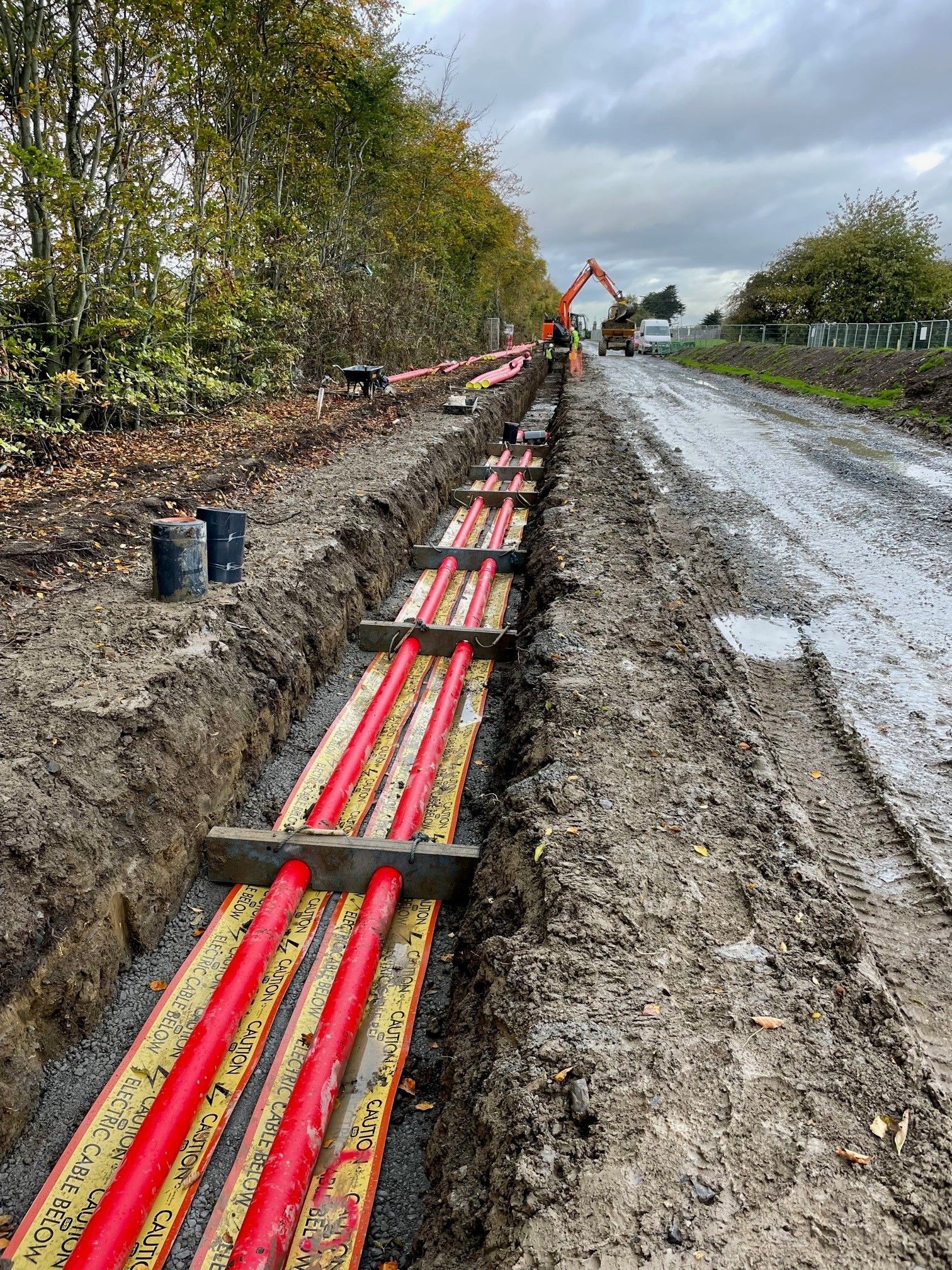 A row of red pipes are being installed in the dirt on the side of a road.