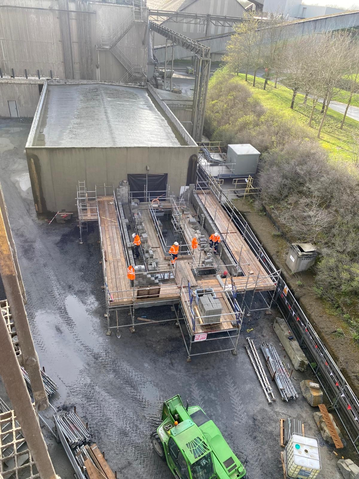 A green truck is parked in front of a building under construction.