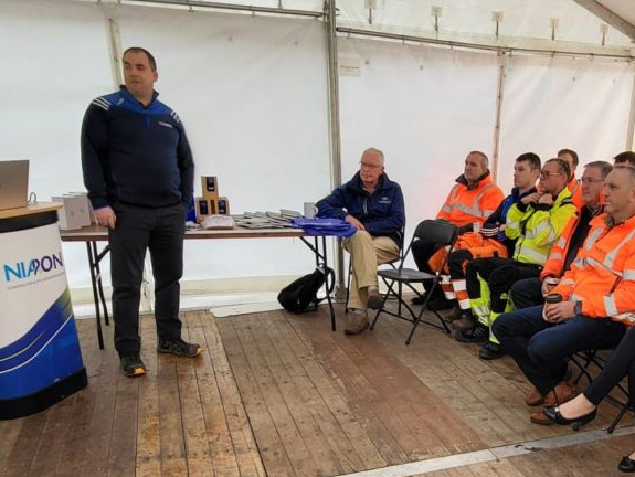 A man is giving a presentation to a group of people in safety vests