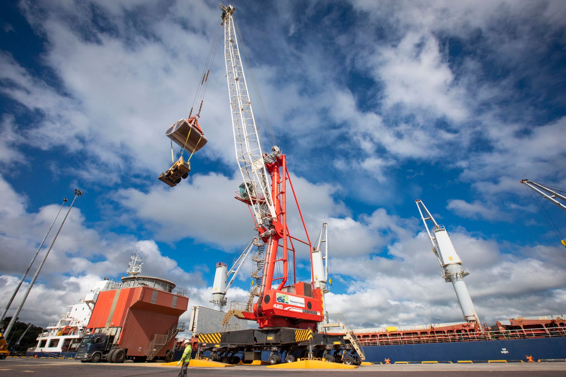 A large red and white crane is lifting a container