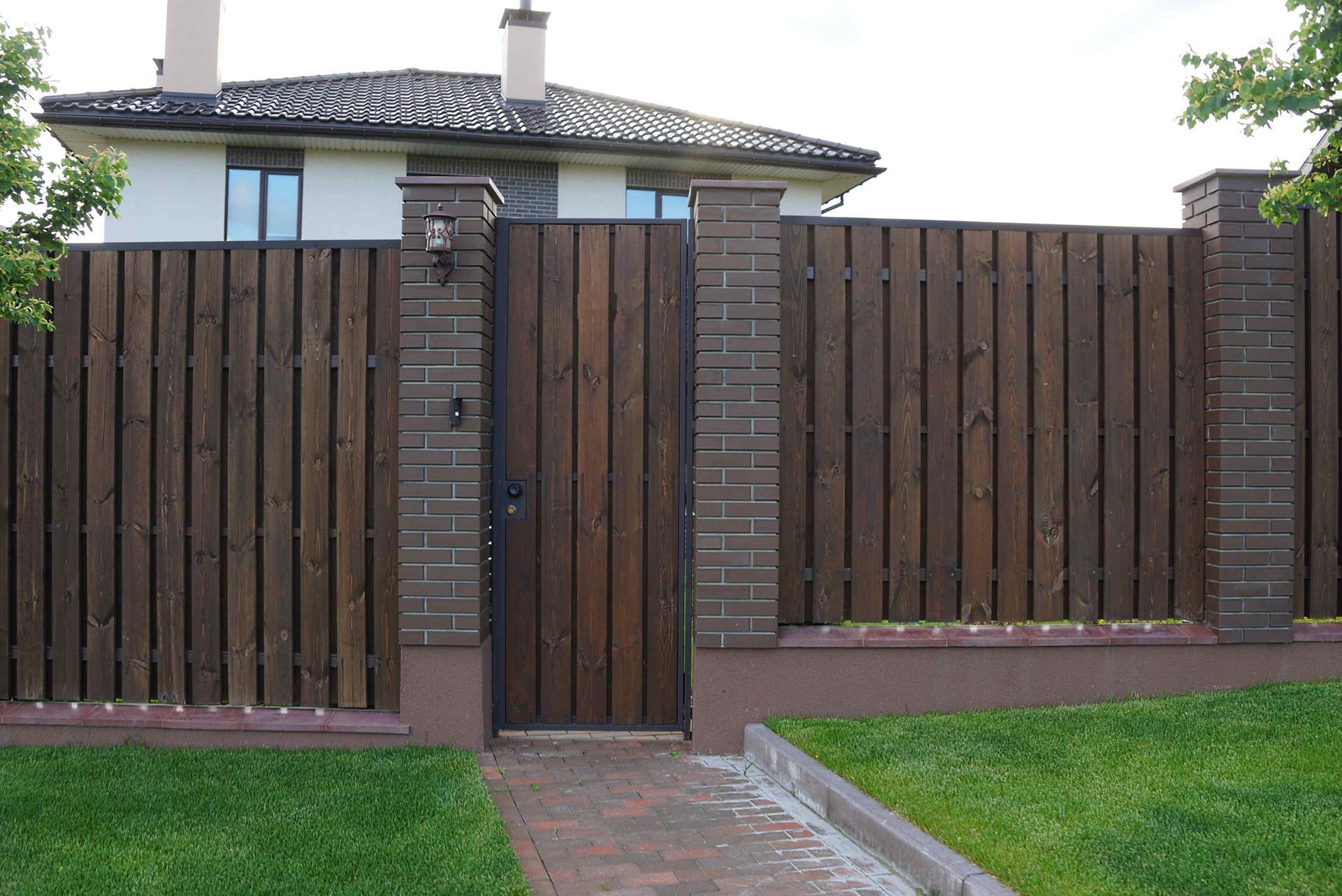 Wooden fence with gate, brick pillars, and house in background.