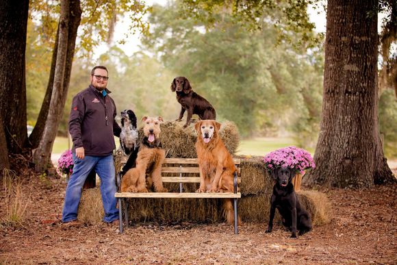a man stands next to a wooden bench with four dogs sitting on it