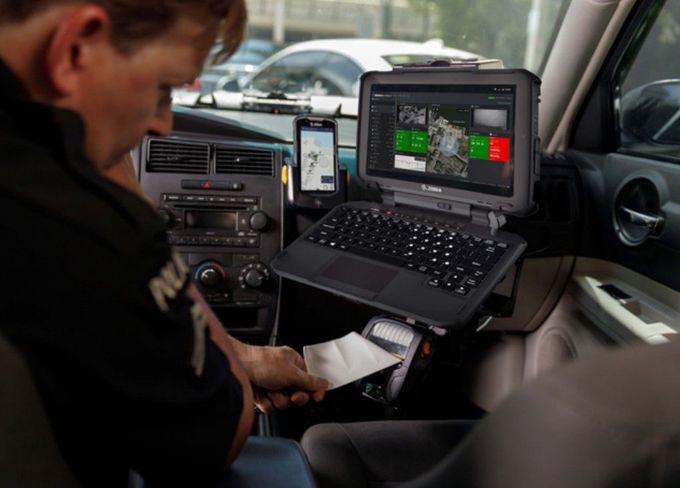 A police officer inside a car uses a mounted laptop, looking at a map with red and green sections.