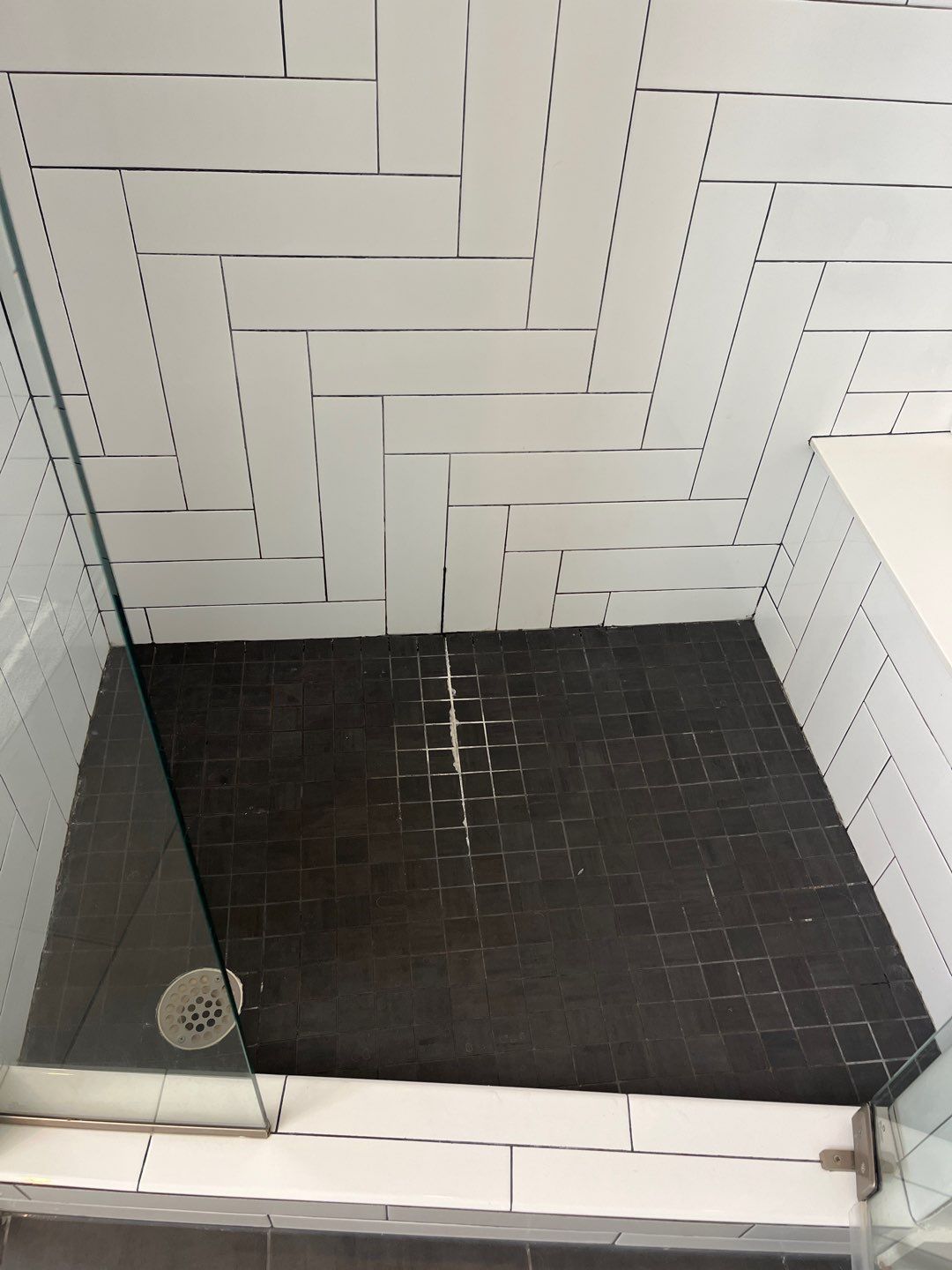 Shower with dark tile floor, white herringbone-patterned wall tiles, and glass enclosure.