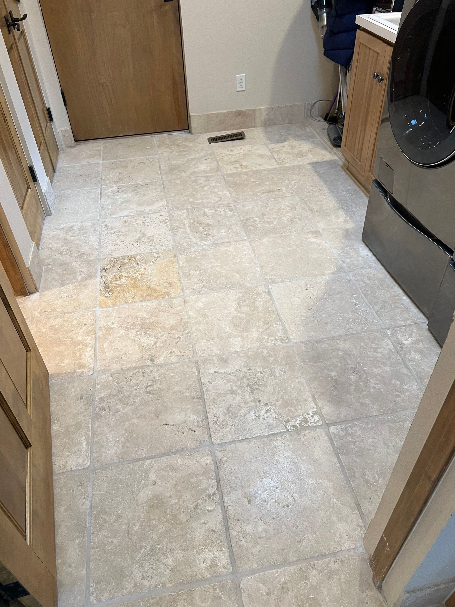 Beige tiled floor in a room with a wooden door, cabinets, and a washing machine.