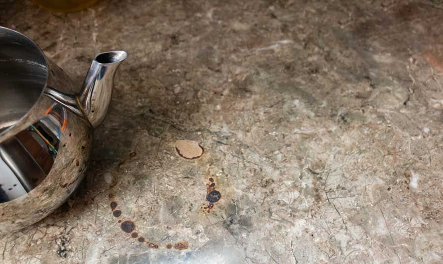 A stainless steel teapot is sitting on a marble counter next to a cup of coffee.