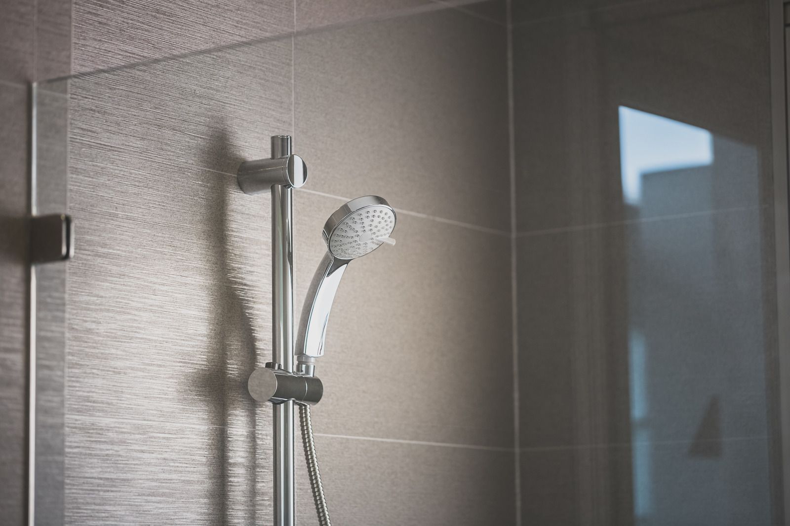 Showerhead on a wall with tiled background and glass panel.