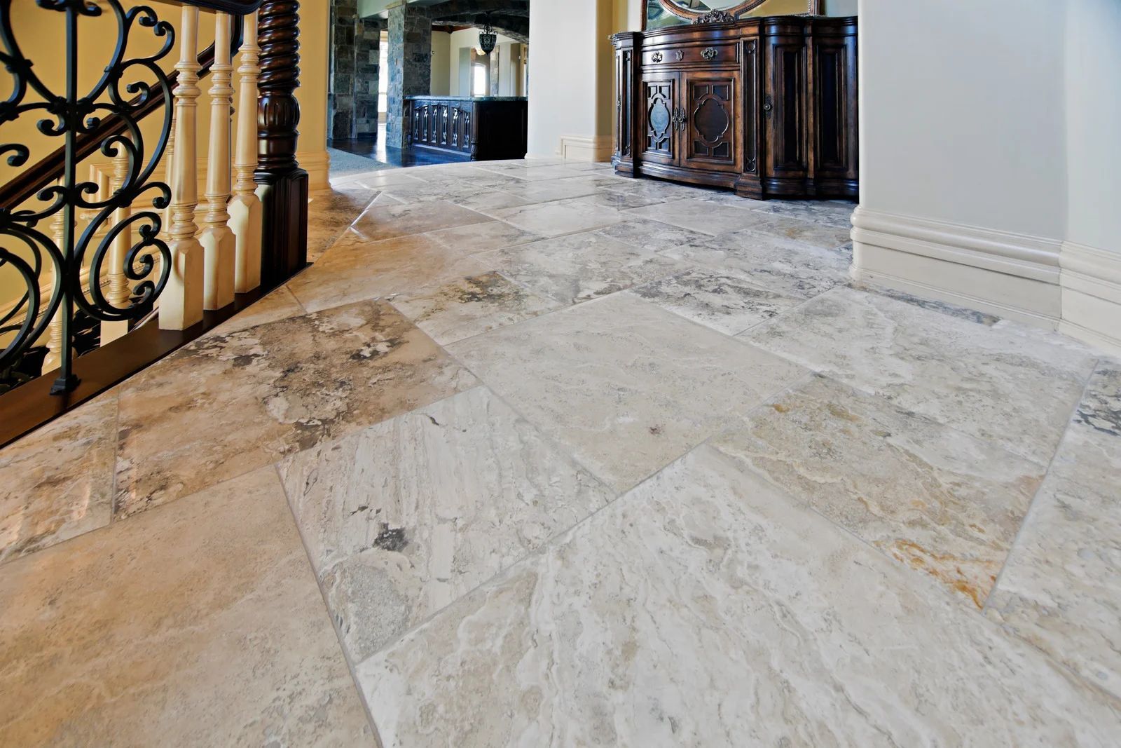 Stone tile flooring in a home hallway with a wooden staircase and ornate railing.