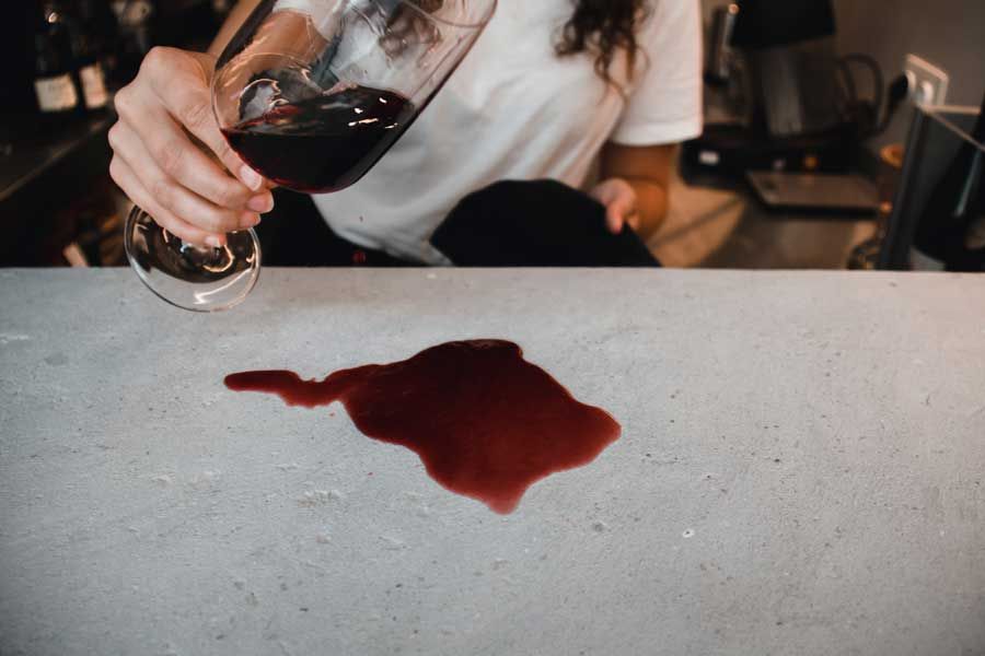 A woman is pouring a glass of red wine on a counter.