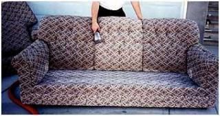 A person is cleaning a couch with a vacuum cleaner.