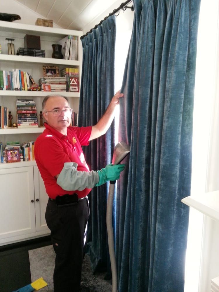 A man in a red shirt is cleaning blue curtains