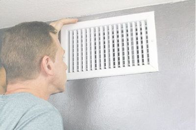A man is looking at a vent on the wall.