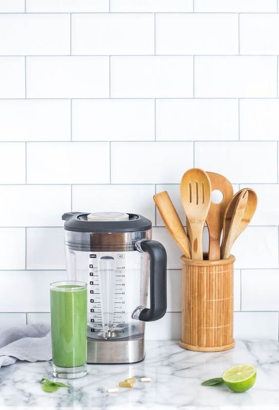 A blender is sitting on a counter next to a glass of green smoothie.