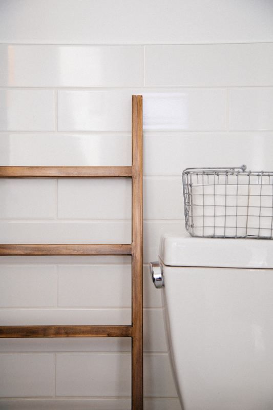 A wooden ladder is next to a toilet in a bathroom.