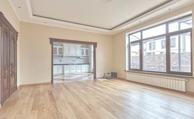 An empty living room with hardwood floors and a kitchen in the background.