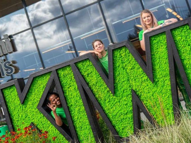 En gruppe mennesker står foran et stort grønt skilt som sier kiwi.