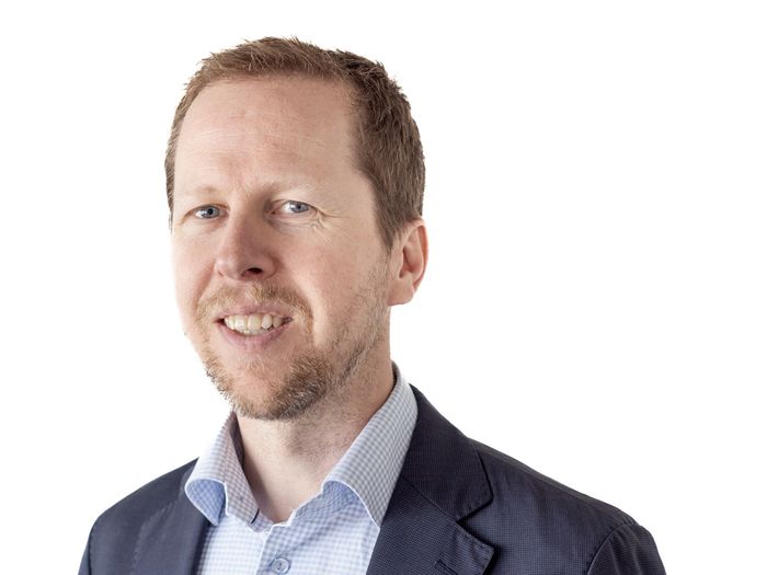 En mann med skjegg har på seg dress og smiler.