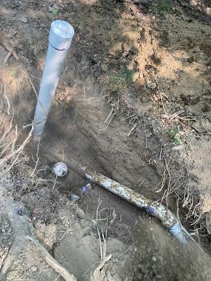 A pipe is laying in the dirt next to a pole.