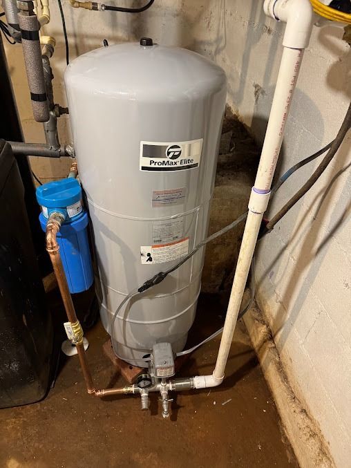 A water tank is sitting next to a pipe in a basement.