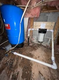 A blue water tank is sitting next to a white pipe in a basement.